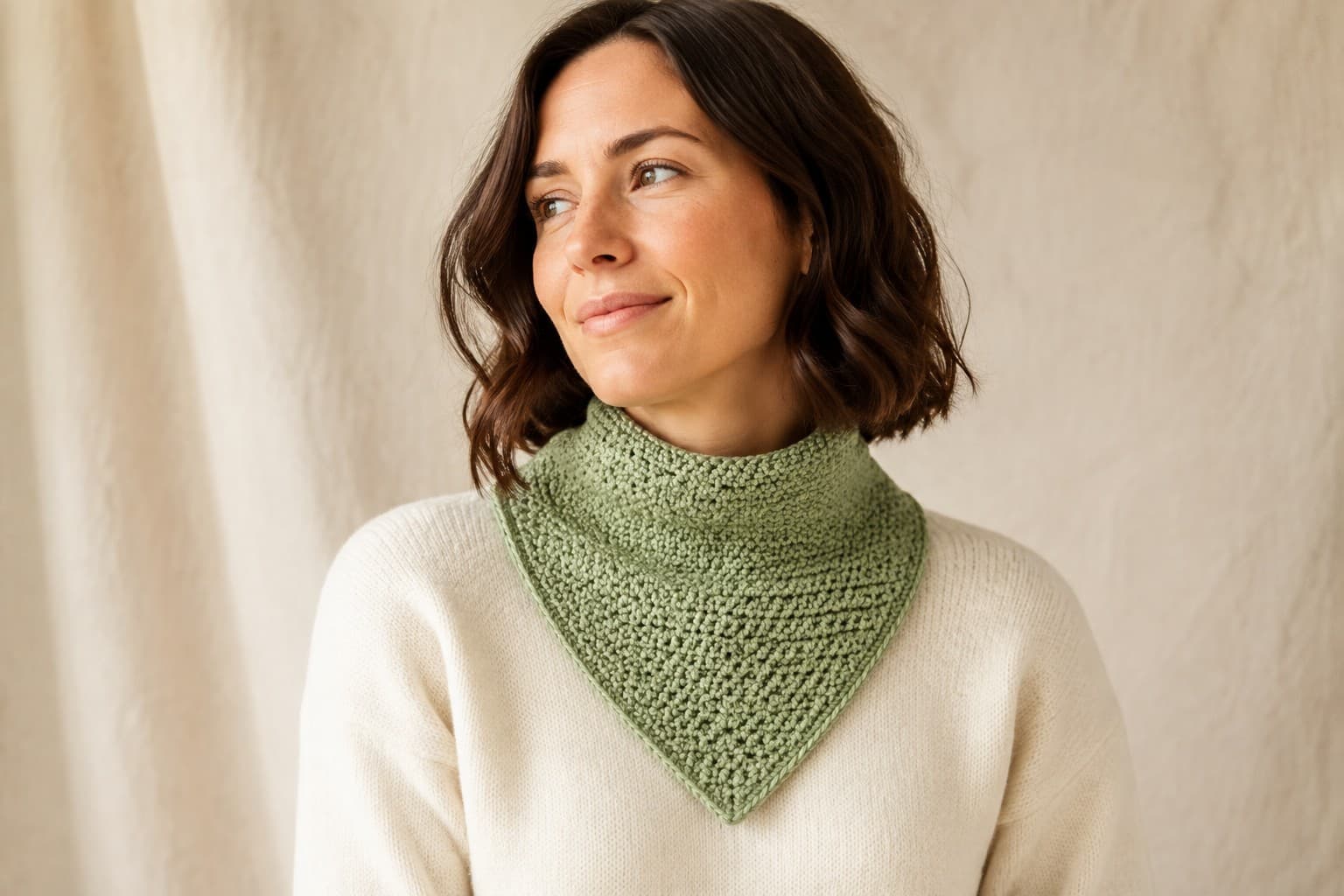 Adult wearing a sage-green seamless crochet bandana cowl with a centered pointed front