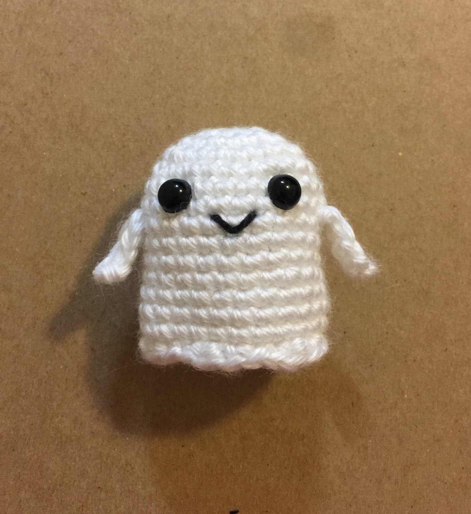 Actual tiny white crochet ghost sample with black eyes, slim arms and a stitched smile.