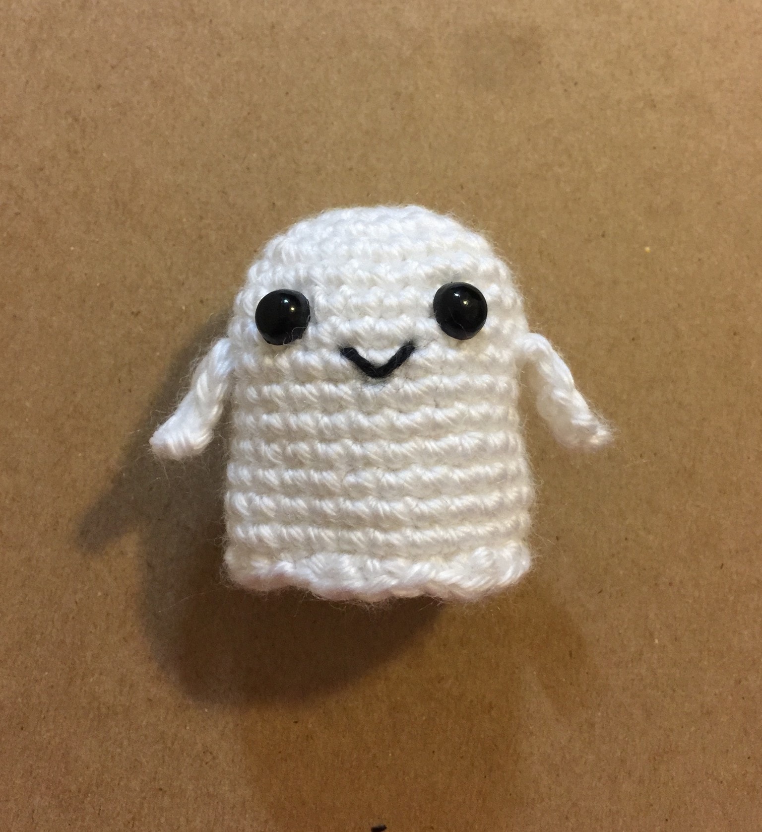 Actual tiny white crochet ghost sample with black eyes, slim arms and a stitched smile.